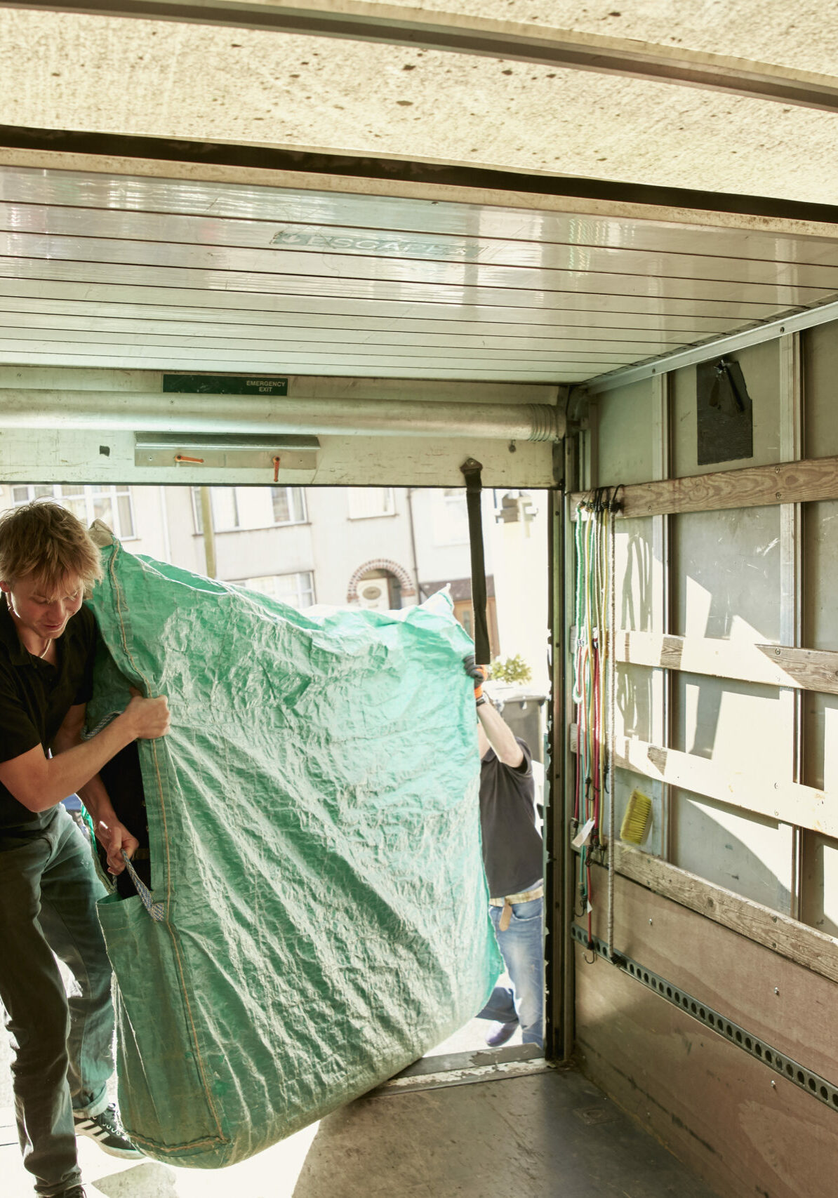 Removals business. A man lifting an item of furniture covered in green plastic into a removals van.